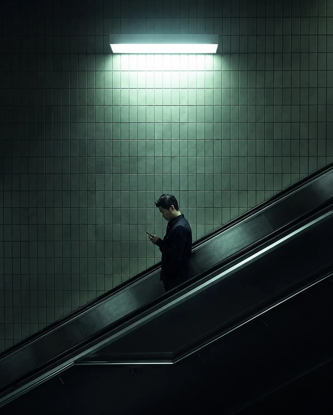 A man reading on his phone while riding a subway escalator